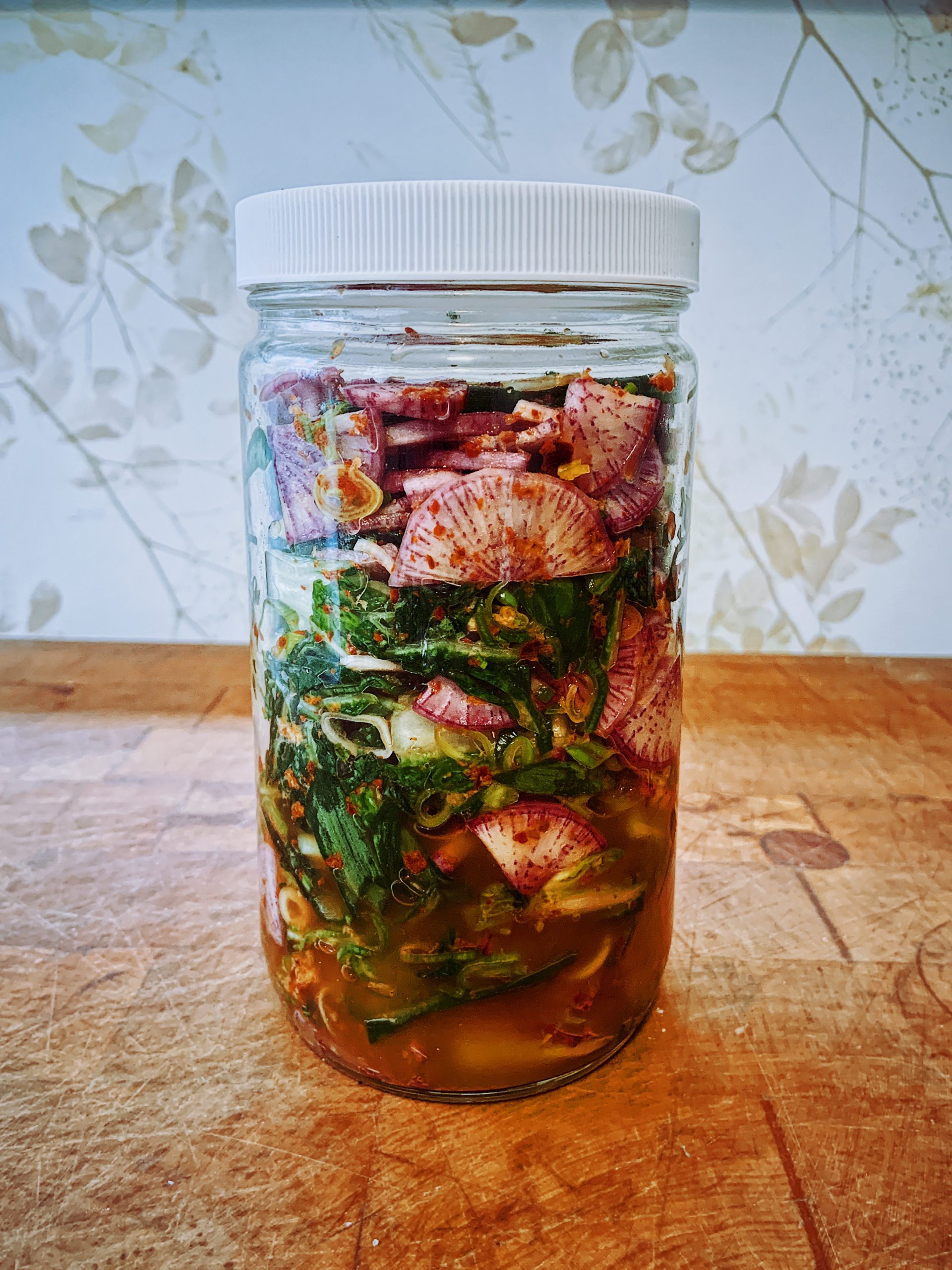 A Mason Jar  on a butcher block in the process of pickling Daikon & Green Garlic Kimchi. Recipe by Michael Joyce with Taproot Farm, PA.