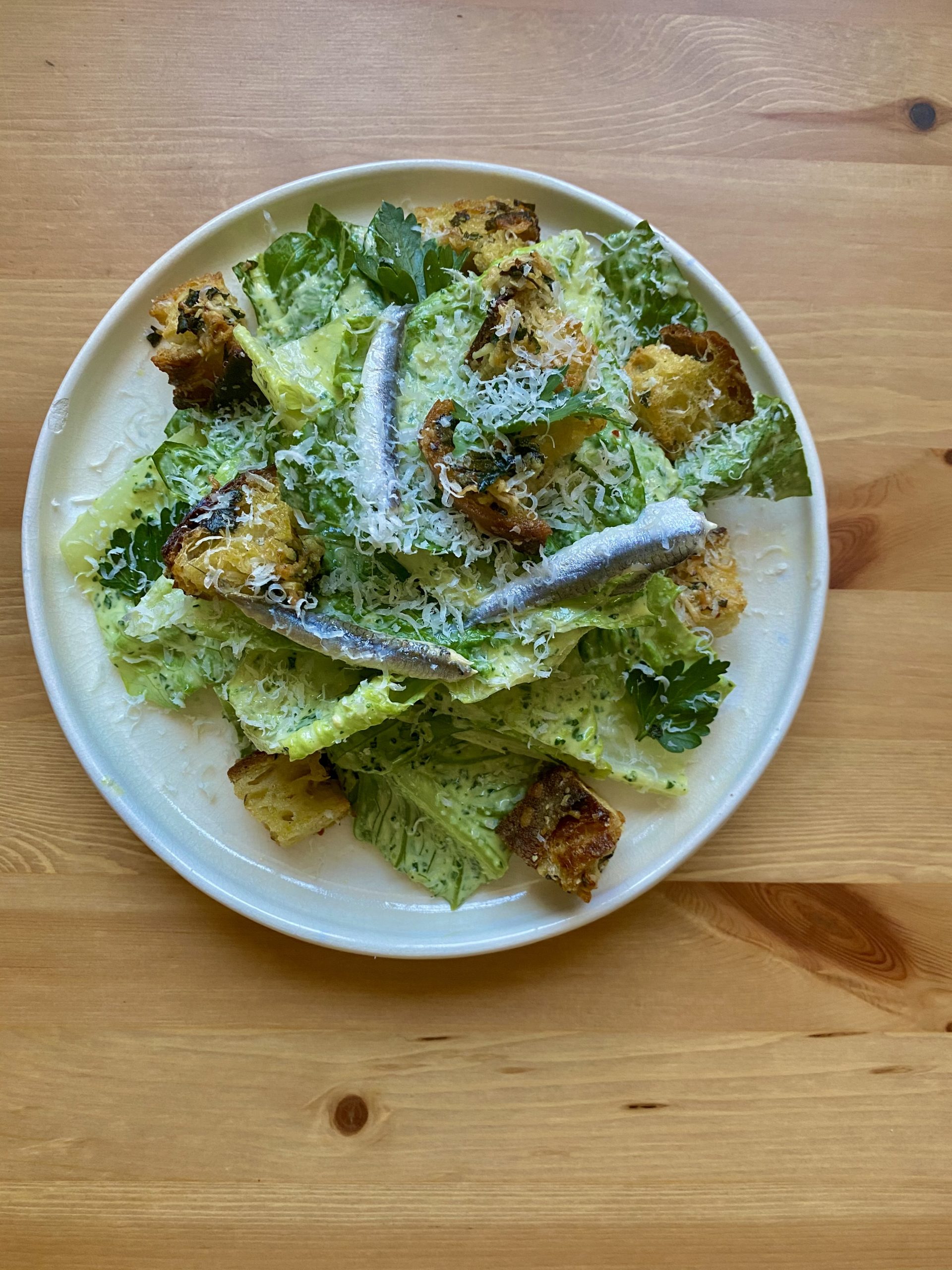 A caesar salad with anchovy and croutons on top.