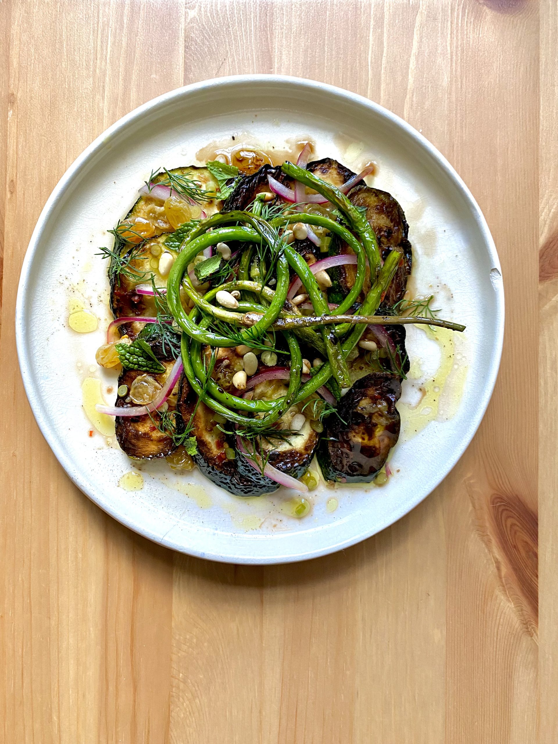 A plate with a zucchini appetizer, including onions, spices, herbs, and garlic scapes.
